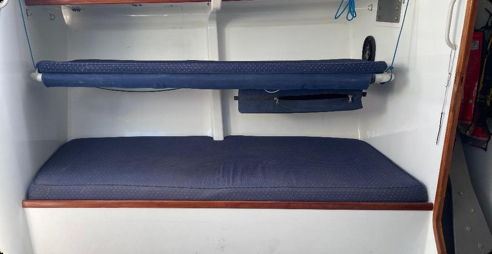 Starboard pipe cot with blue cushion and a rolled bunk board above